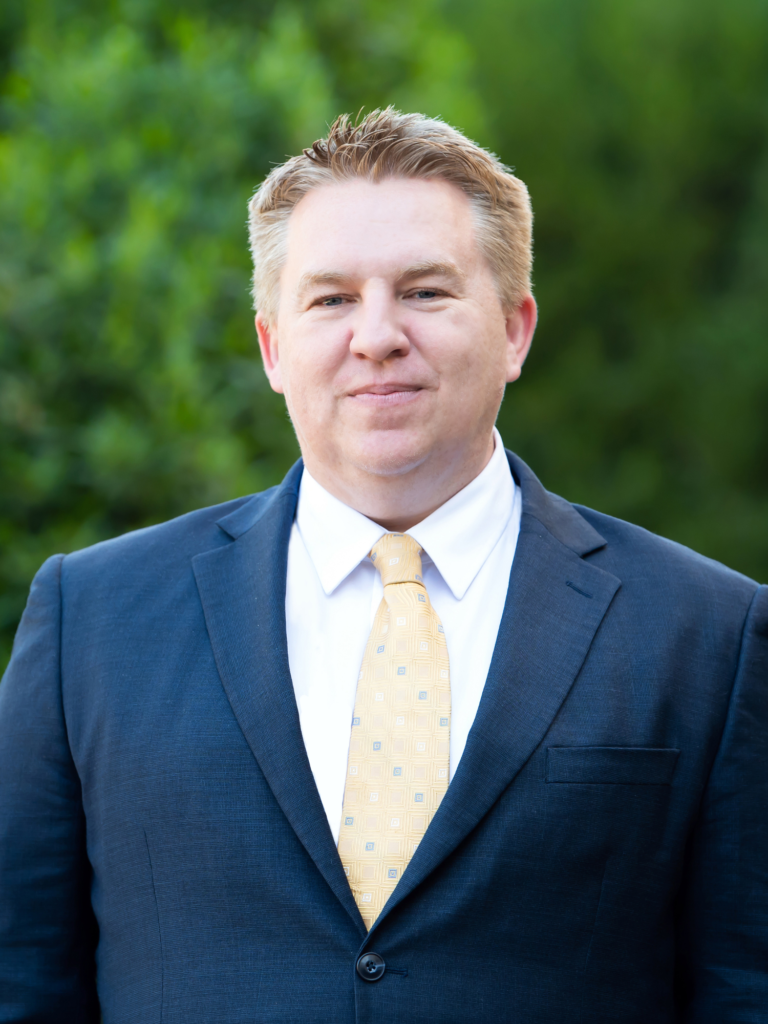 Daniel Nigh, Attorney and Partner at Nigh Goldenberg Raso & Vaughn, PLLC, smiling in front of a garden backdrop.