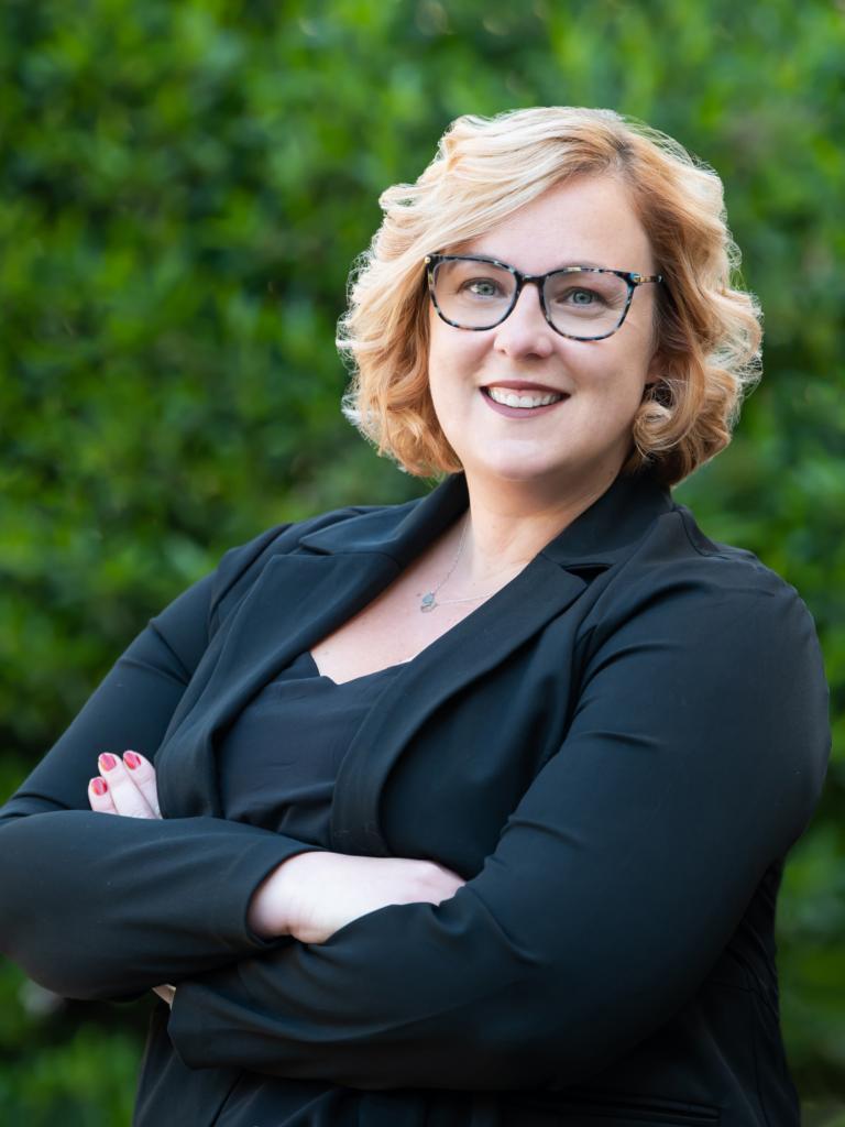 Ashleigh Raso, Attorney and Partner at Nigh Goldenberg Raso & Vaughn, PLLC, smiling in front of a garden backdrop."