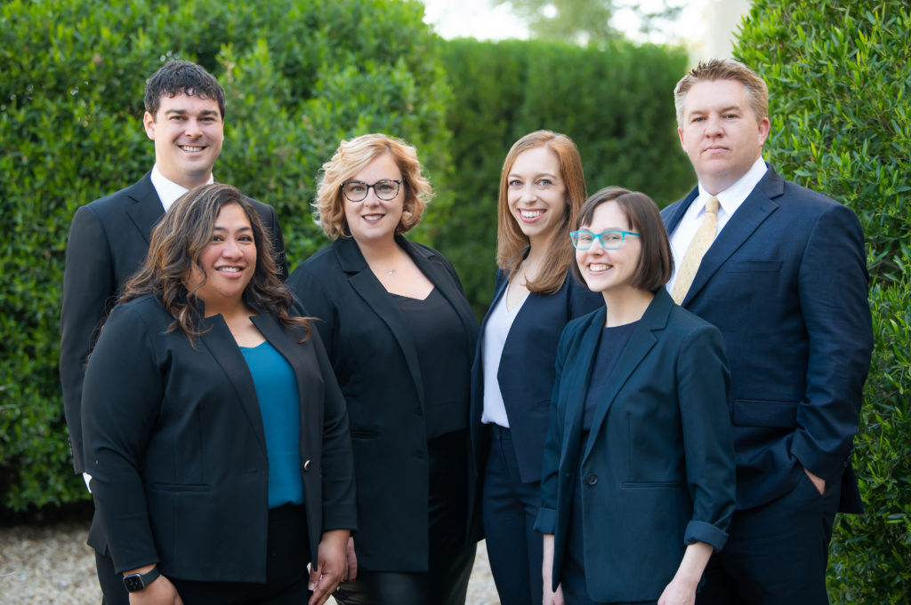 Daniel Nigh, Marlene Goldenberg, Ashleigh Raso, Brett Vaughn, Sam Hoefs, and Ava Cavaco, Attorneys at Nigh Goldenberg Raso & Vaughn, PLLC, smiling in front of a garden backdrop.